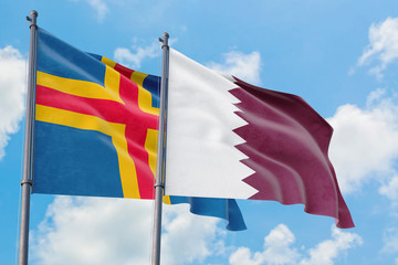 Qatar and Aland Islands flags waving in the wind against white cloudy blue sky together. Diplomacy concept, international relations.