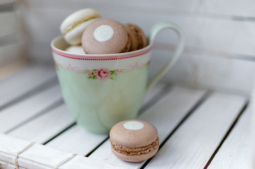 French colourful macarons in a green vintage mug, partial blur..Cup of macarons on a light wood background. Concept about love.