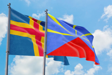 Reunion and Aland Islands flags waving in the wind against white cloudy blue sky together. Diplomacy concept, international relations.