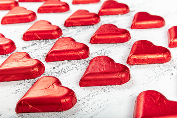 Chocolate heart in red foil. Valentine's day on white wooden background for texture.