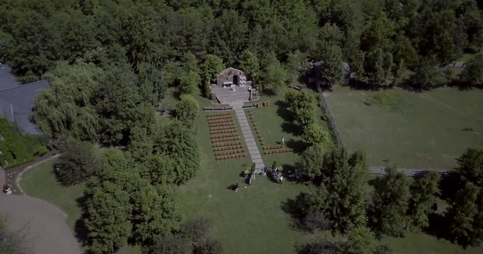Chairs and decorations being setup for an outdoor wedding ceremony at a Stone Chapel in the forest. Orbiting Aerial Drone