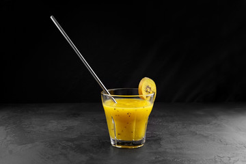 Kiwi gold fruit juice in transparent glass with steel straw on stone table on black background. Fresh yellow kiwi smoothie with cocktail tube. Healthy drink