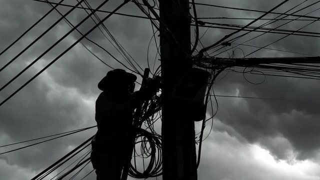 Silhouette of technician in protective gear on a ladder installing optical fiber cables.