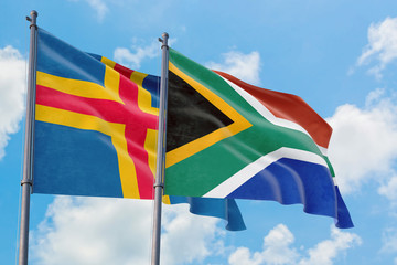 South Africa and Aland Islands flags waving in the wind against white cloudy blue sky together. Diplomacy concept, international relations.