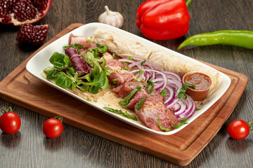 Barbecue on a white plate and a wooden cutting Board with sauce and onions