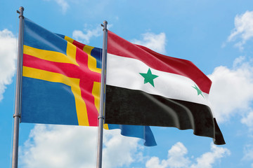 Syria and Aland Islands flags waving in the wind against white cloudy blue sky together. Diplomacy...