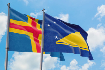 Tokelau and Aland Islands flags waving in the wind against white cloudy blue sky together. Diplomacy concept, international relations.