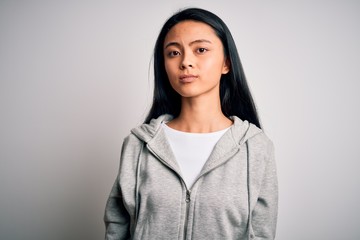 Obraz premium Young beautiful chinese sporty woman wearing sweatshirt over isolated white background Relaxed with serious expression on face. Simple and natural looking at the camera.