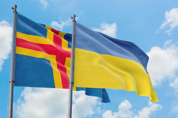 Ukraine and Aland Islands flags waving in the wind against white cloudy blue sky together. Diplomacy concept, international relations.