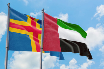 United Arab Emirates and Aland Islands flags waving in the wind against white cloudy blue sky together. Diplomacy concept, international relations.