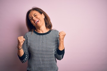 Middle age beautiful woman wearing casual sweater standing over isolated pink background very happy...