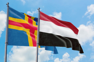 Yemen and Aland Islands flags waving in the wind against white cloudy blue sky together. Diplomacy concept, international relations.