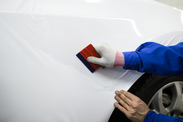 Obraz premium Car wrapping specialist putting vinyl foil or film on car. Selective focus.