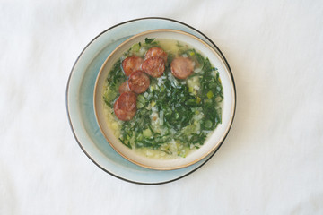 Caldo Verde Soup with greens and chopped chorizo on the top in ceramic bowl.