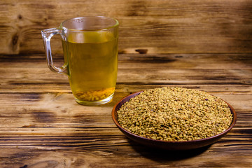Cup of yellow tea (methi dana) and plate with fenugreek seeds on wooden table