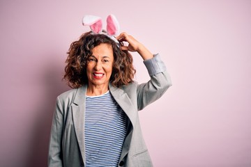 Middle age beautiful woman wearing bunny ears standing over isolated pink background confuse and...