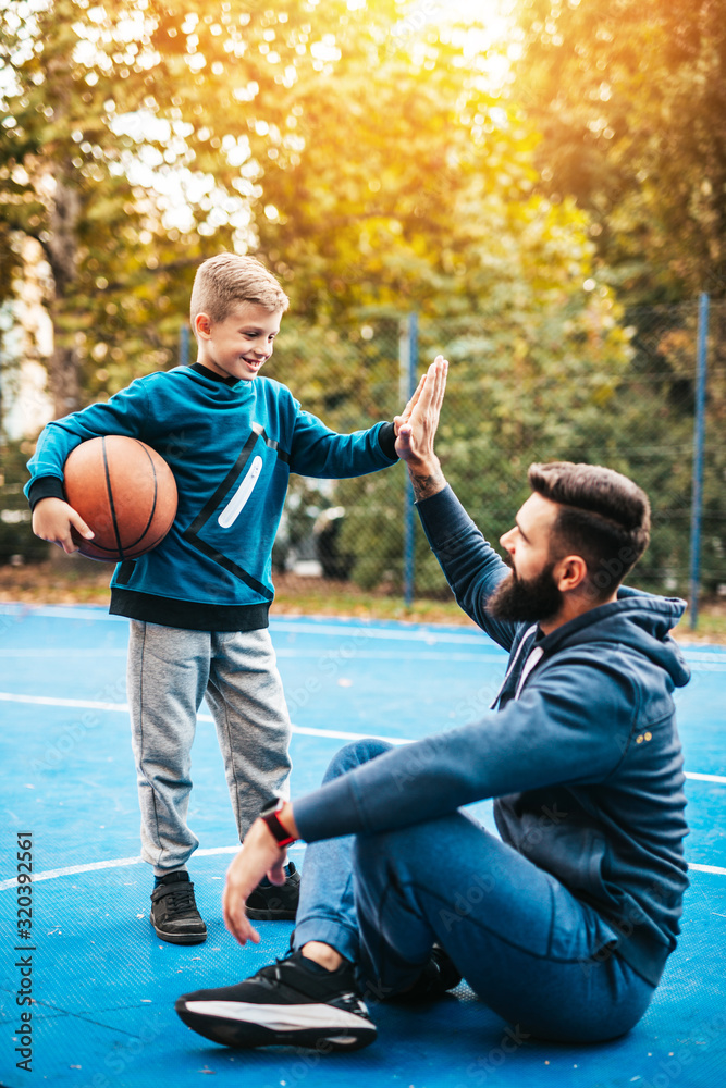 Wall mural father and his son enjoying together on basketball court.