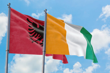 Cote D'Ivoire and Albania flags waving in the wind against white cloudy blue sky together....
