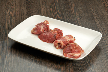 portions of raw meat on a white plate on a wooden table