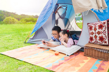 couple asian children stay on floor and rest in tent, they camping and picnic on nature background, asian boy playing smartphone, they feeling happy and smile in relax time