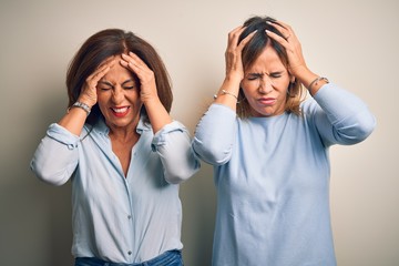 Middle age beautiful couple of sisters standing over isolated white background suffering from headache desperate and stressed because pain and migraine. Hands on head.