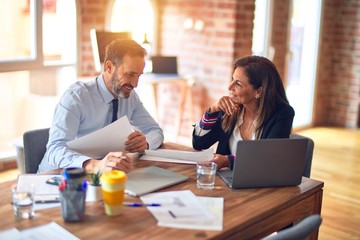 Two middle age business workers smiling happy and confident. Working together with smile on face using laptop at the office