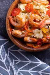 Farfalle pasta with shrimp and spinach and cherry tomatoes in a wooden plate