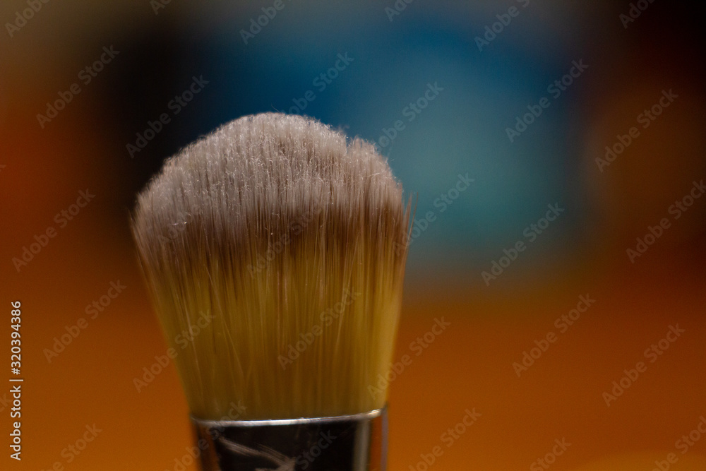 Wall mural close-up makeup brush on blurred colored background.