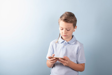 a boy plays a smart phone in wireless headphones on a blue background, concept of children gadgets addiction