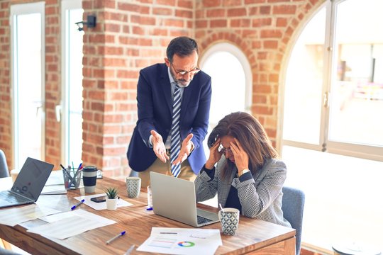 Two middle age business workers working together. Man bullying woman at the office