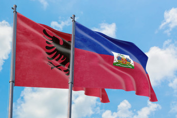 Haiti and Albania flags waving in the wind against white cloudy blue sky together. Diplomacy concept, international relations.
