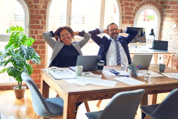 Two middle age business workers smiling happy and confident. Working together with smile on face and hands on head in a relaxed moment at the office