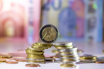 Stapel Euro-Münzen mit stehender 2-EURO-Münze aus 2 Euro, 1 Euro und Cent-Münzen mit einem Haufen Bargeld aus Geldscheinen und EURO-Münzen zeugt von Reichtum in der Finanzwelt und schnelles Geld