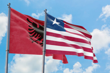 Liberia and Albania flags waving in the wind against white cloudy blue sky together. Diplomacy concept, international relations.