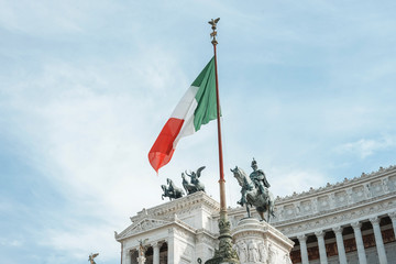 Fototapeta na wymiar View of Italian national flag in front of Altare della Patria (Altar of the Fatherland) , the equestrian sculpture of Victor Emmanuel and statue of the goddess Victoria riding on quadrigas on top.
