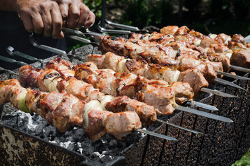 Man Scrolls Skewer with Juicy Pickle Pieces Of Pork or Beef Meat On A Grill.