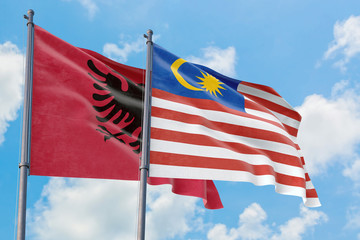 Malaysia and Albania flags waving in the wind against white cloudy blue sky together. Diplomacy concept, international relations.