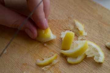 Slicing a lemon into pieces with a knife held by a person's hands. On a wooden background.
