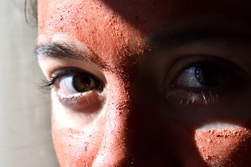 Young pretty-eyed girl with her face covered by a clay mask photographed with natural side light