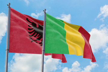 Mali and Albania flags waving in the wind against white cloudy blue sky together. Diplomacy concept, international relations.