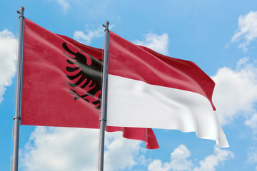 Monaco and Albania flags waving in the wind against white cloudy blue sky together. Diplomacy concept, international relations.