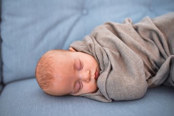 Adorable baby lying down on the sofa over blanket at home. Newborn relaxing and sleeping comfortable