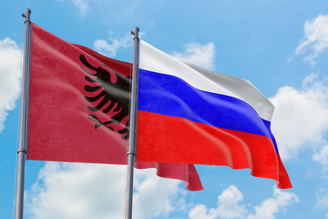 Russia and Albania flags waving in the wind against white cloudy blue sky together. Diplomacy concept, international relations.