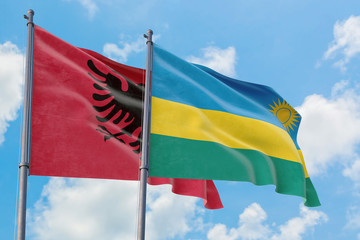 Rwanda and Albania flags waving in the wind against white cloudy blue sky together. Diplomacy concept, international relations.