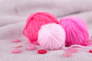 Pink balls of yarn of different sizes and buttons on a gray knitted background. Handicraft, needlework, hobby, knitting, DIY