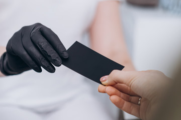 doctor's hands dressed in black sterile gloves pass a black business card into the client's hand...