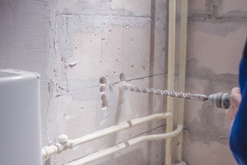 a man working in a white helmet with a large perforator drills a light wall, copy space; space for text