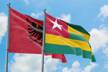 Togo and Albania flags waving in the wind against white cloudy blue sky together. Diplomacy concept, international relations.