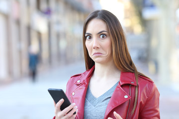 Perplexed woman using phone looks at camera