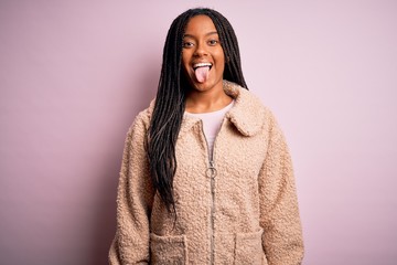 Young african american woman wearing fashion winter coat over pink isolated background sticking tongue out happy with funny expression. Emotion concept.